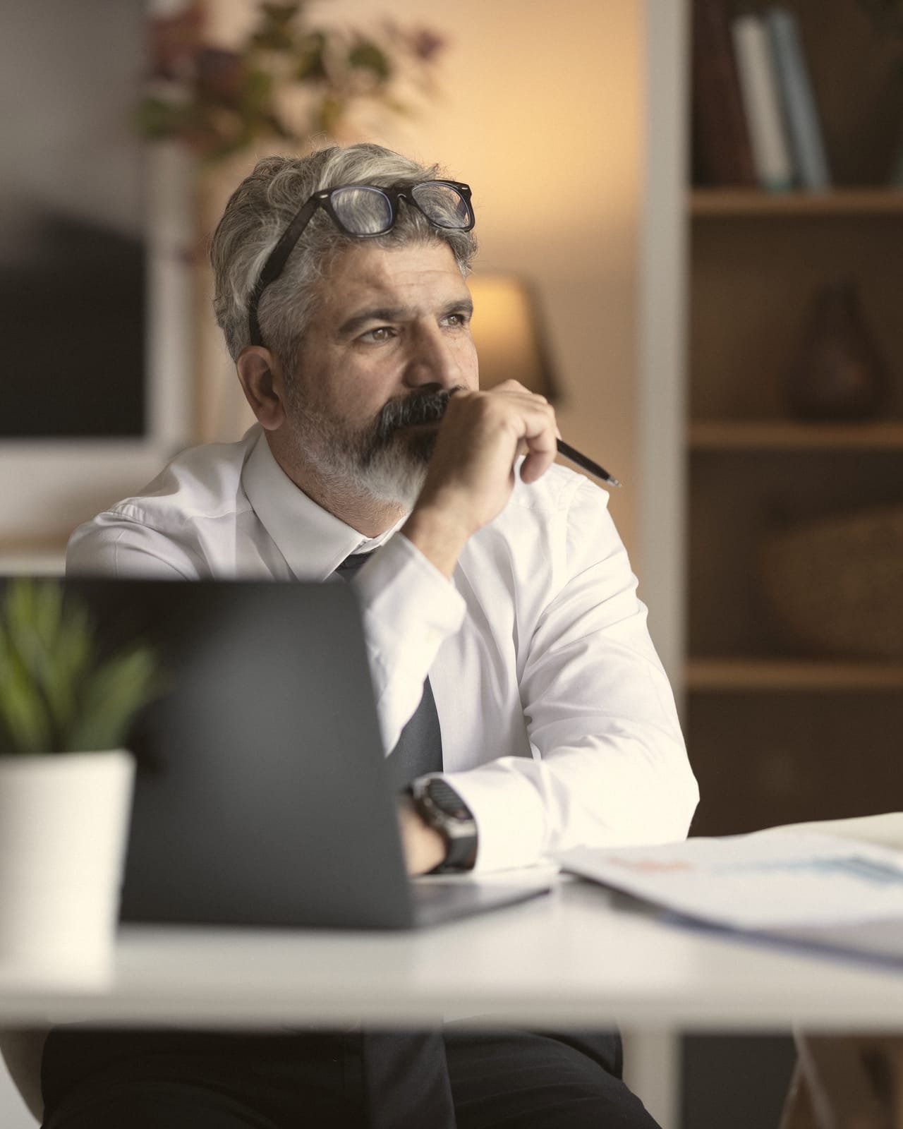 Dirigeant en réflexion dans un bureau de domaine ou une salle de réunion : documents sur la table, lumière naturelle chaude.